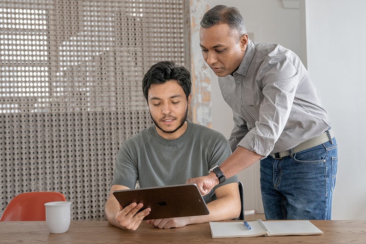 Two men in an office behind a wooden table looking at a tablet that contains their business’s OKR templates.