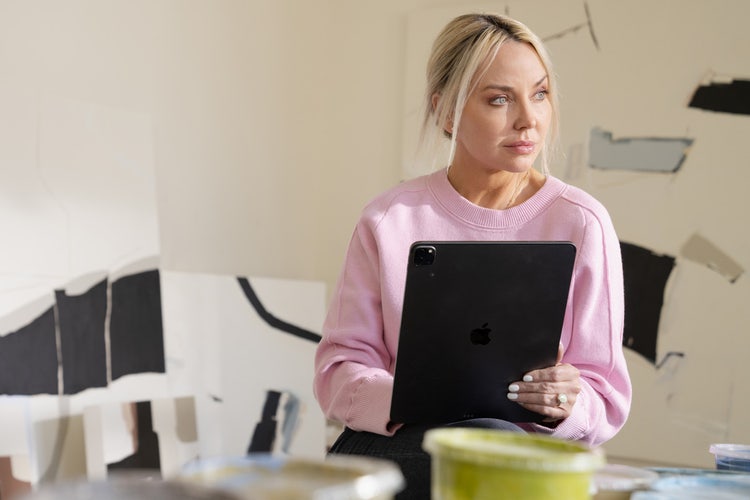 Person wearing a pink sweatshirt in an art studio working on a black tablet to set up a business and enjoy the advantages of sole proprietorship.