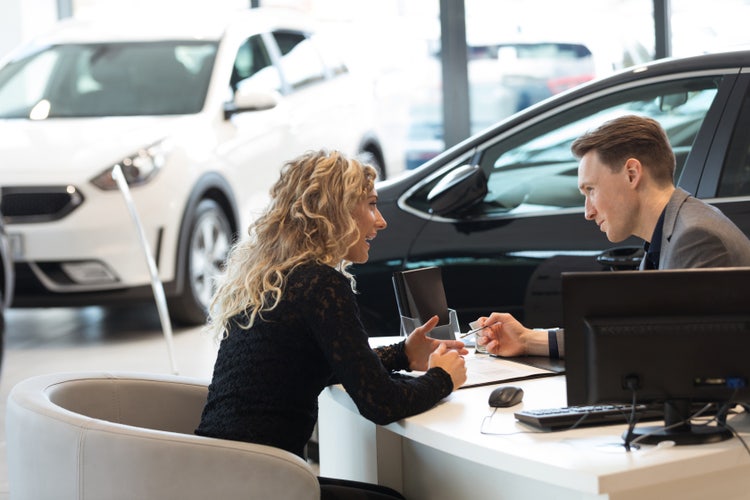 A woman and a car salesman at a dealership go through dealer invoice before signing it.