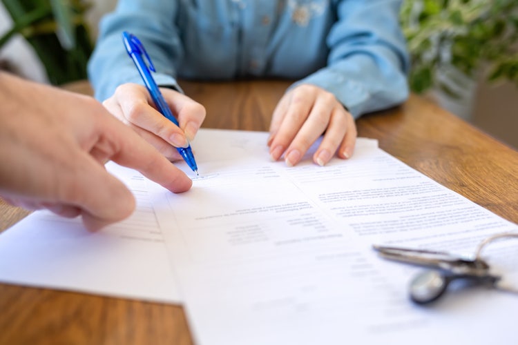 A woman holding a pen signs an as is bill of sale form.