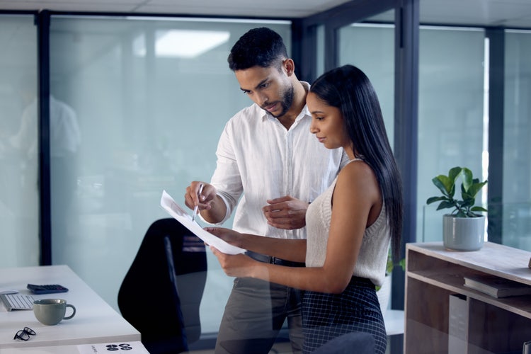 A man and woman in a office look over a bill of sale.