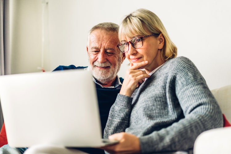 A man and woman sitting next to each other use electronic health records software on a laptop.