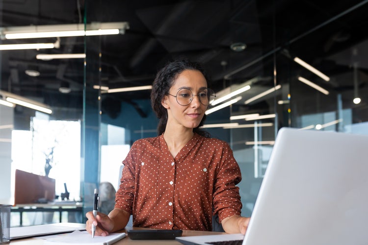 A woman in an office uses her laptop to write an invoice for freelance work