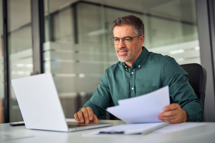 A man in an office uses his laptop to learn what an "as is" real estate contract is.