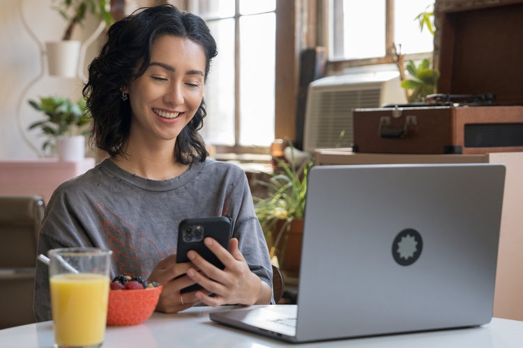 Person sitting at a breakfast table with laptop open and a red bowl and a glass of orange juice, working on their phone learning how to fill out a receipt book.