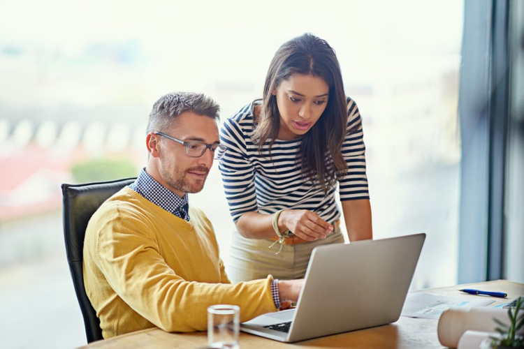 Two co-workers use NDA management software and read a document on a laptop.