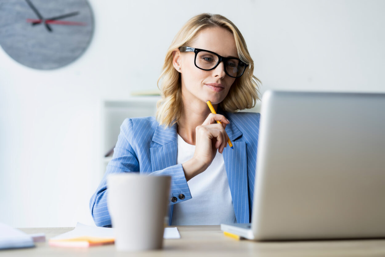 A woman sitting at a table holds a pencil while looking at a laptop to set up a document signing order.