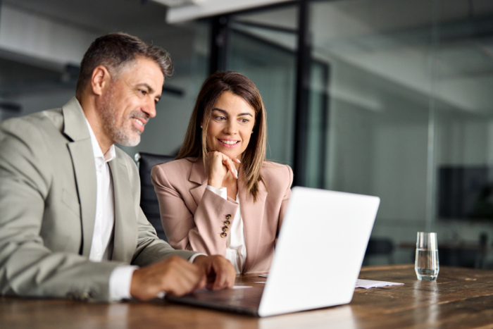 A man and woman sitting at a table look at a contract on a laptop.