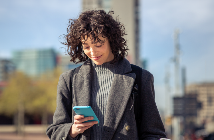 A woman with short brown curly hair and a gray overcoat creates an e-signature using her mobile device.