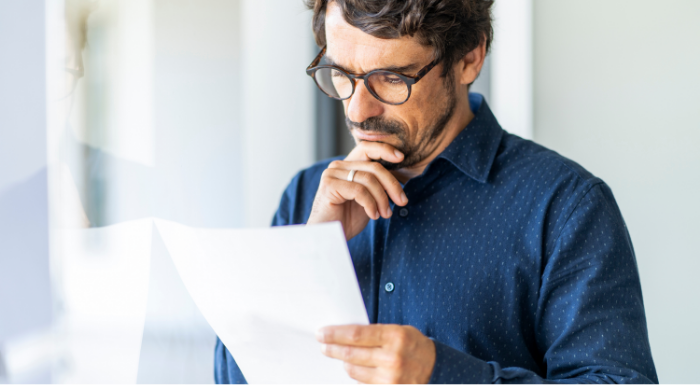 A man with his hand on his chin holds and looks at a piece of paper.