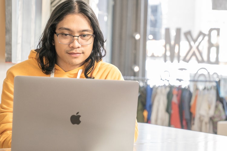 Person in a yellow sweatshirt writing a thank you email after interview template PDF on a silver Apple Mac laptop.