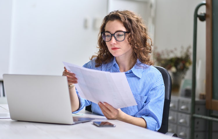 A woman reviewing several bills of sale as examples before handwriting one herself.