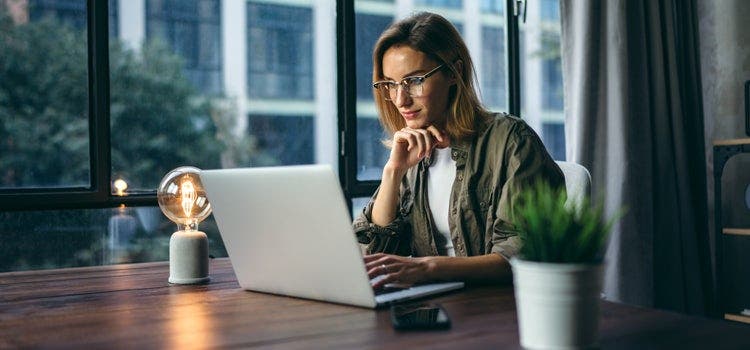 A young professional person wearing glasses working on a laptop to compress a PDF.