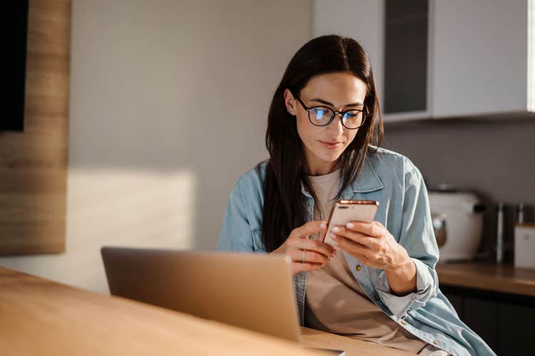 A woman sitting at a kitchen bar area looks at her smartphone.