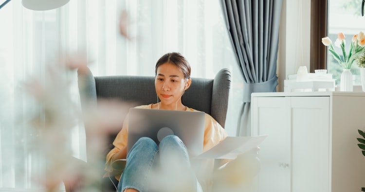 A woman using remote work software while sitting in a chair and using a laptop.