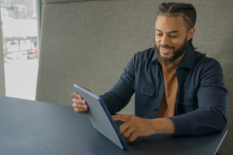 Person in an office wearing an open blue buttoned-down shirt writing a landlord reference letter on a tablet.