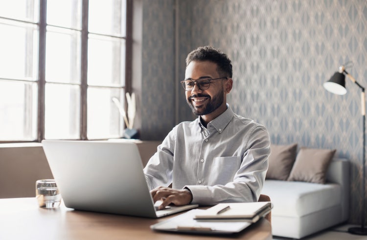 A man in an office uses a laptop to list his certifications on his resume.