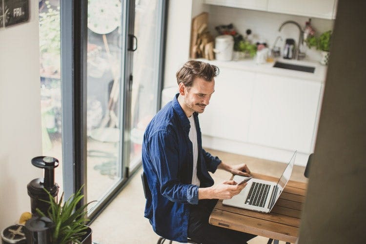 A man uses a phone and a laptop to convert a PDF into an image file.