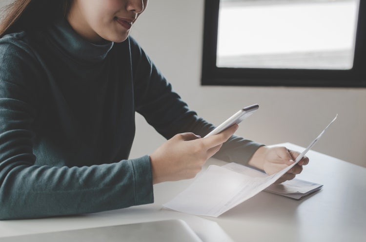 A woman sitting at a table uses document digitization software on her phone to scan a paper document.