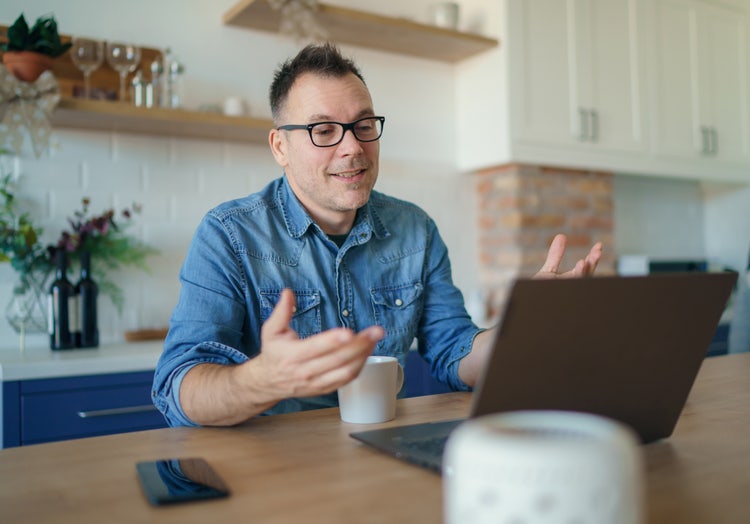 A man sitting at a table collaborates with his remote team on his laptop.