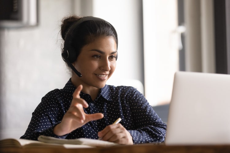 A woman wearing headphones smiles while gesturing and looking at a laptop screen.