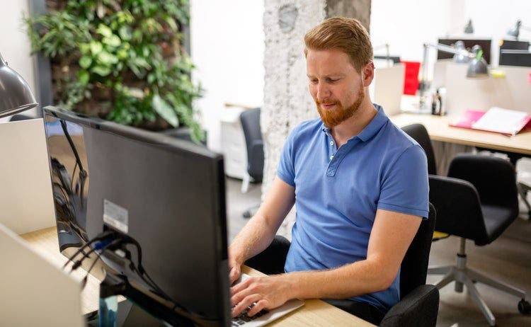 A male office worker wearing a blue shirt deletes PDF files in Windows 10.