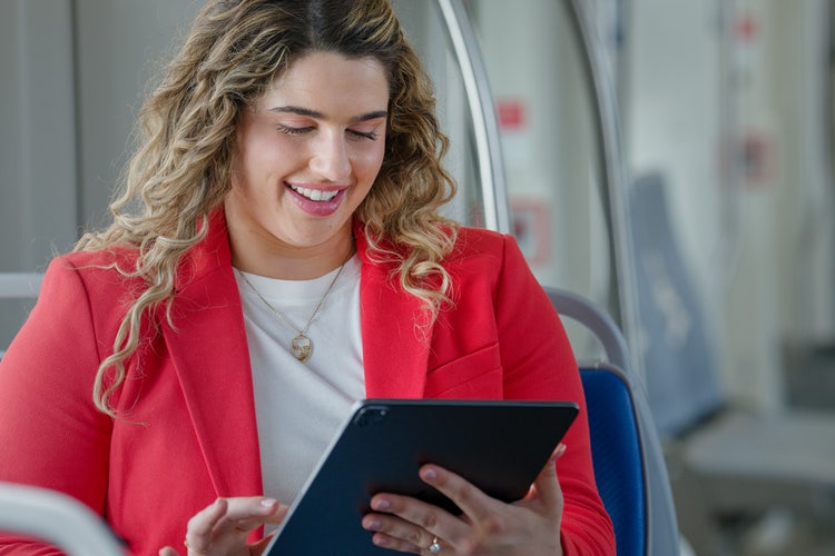 A woman in a red blazer and white top smiles as she learns how to change a PDF size by reading an article on her tablet.