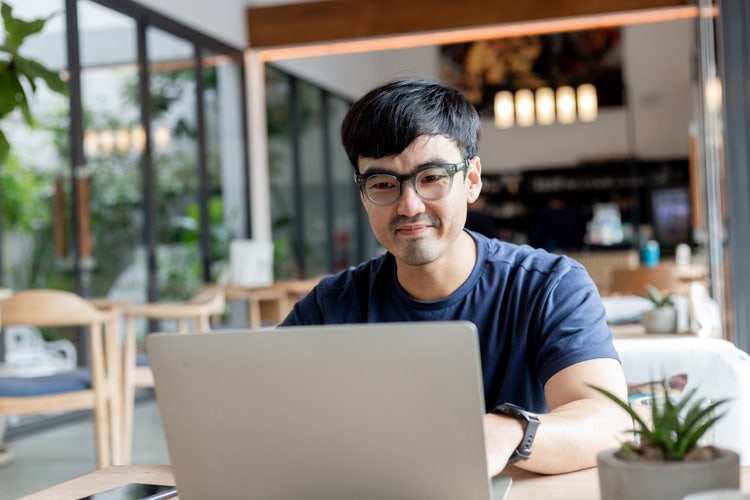 An employee working remotely on his laptop in a cafe as part of the hybrid work model.