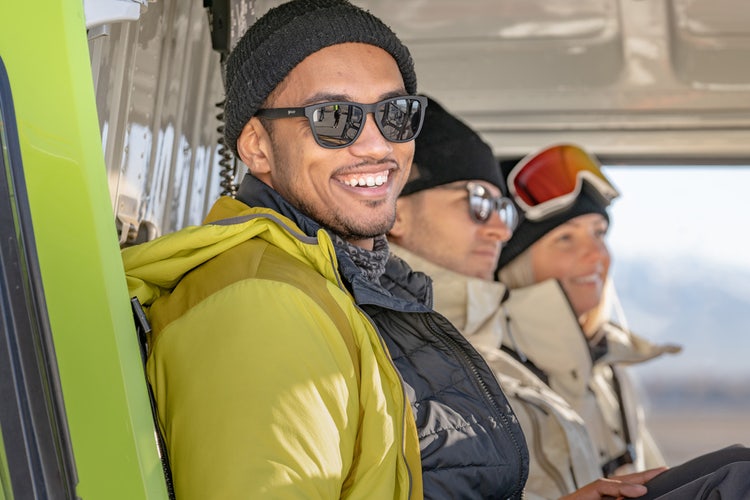 Three people wearing cold-weather clothing and sunglasses having fun on a trip after completing their vacation packing list.