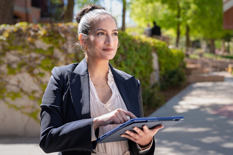 Woman in a blazer walking on the sidewalk holding a tablet and learning how to open a PDF in Chrome web browser.