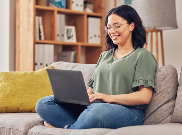 A woman sitting on a couch uses her laptop to write a bill of sale for a used car.