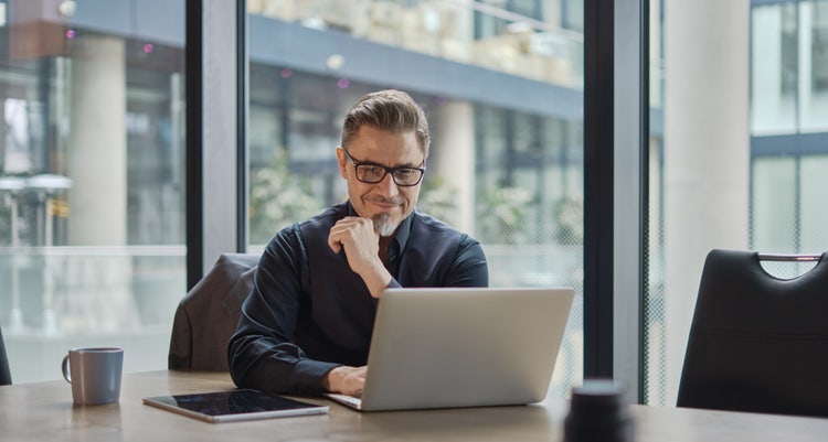 A man in an office uses his laptop to learn how to create a QR code from a PDF.