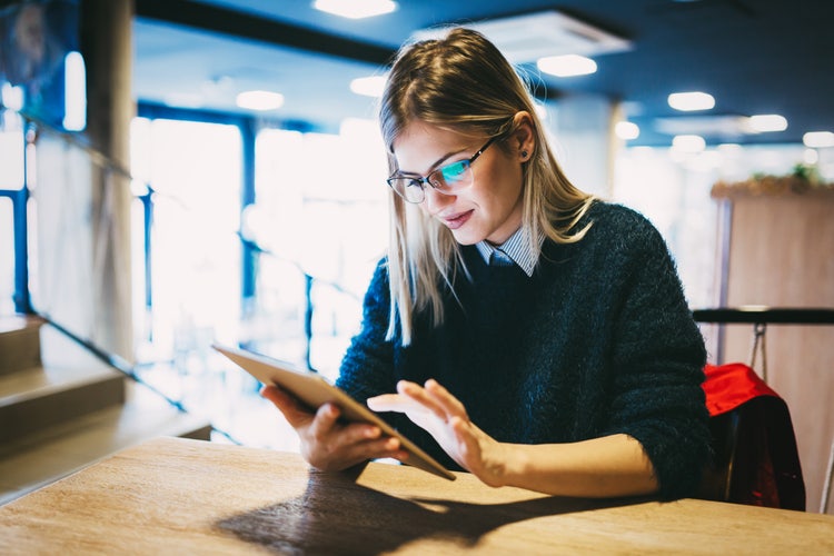 A woman sitting at a table reviewing a document signature on a tablet.