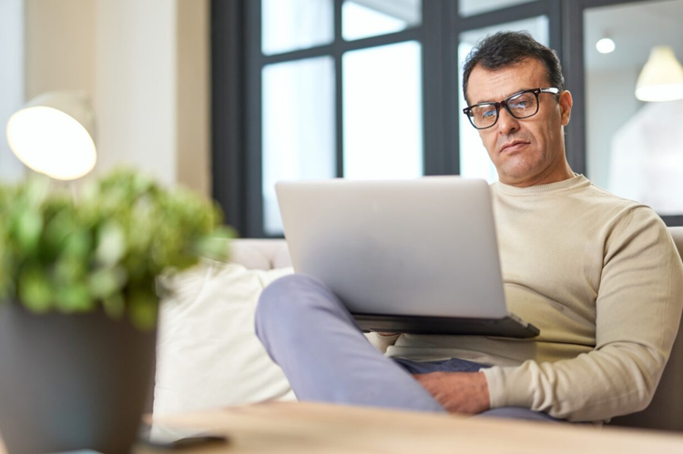 A man sitting on a couch learns about signature loans on his laptop.