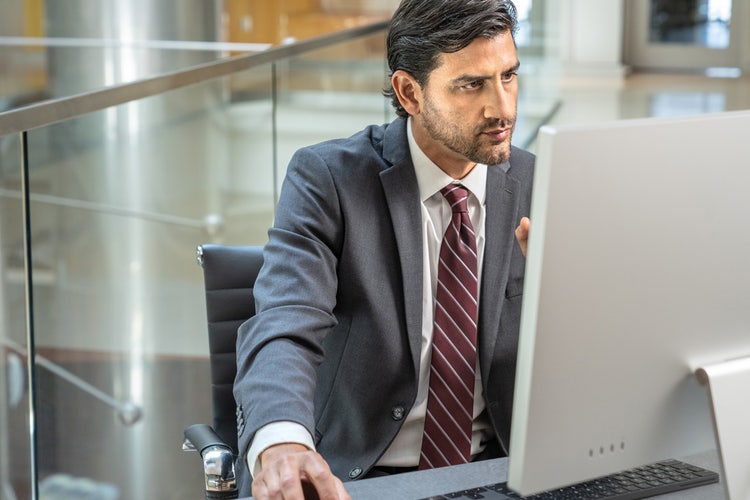 Person wearing a grey business suit and red striped necktie working at a computer to chat with PDF using Acrobat AI Assistant.