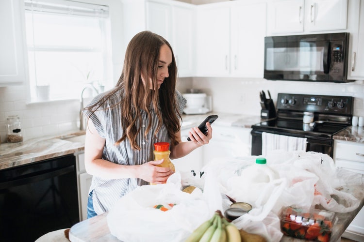 A woman learns how to budget groceries using her cell phone in a kitchen.