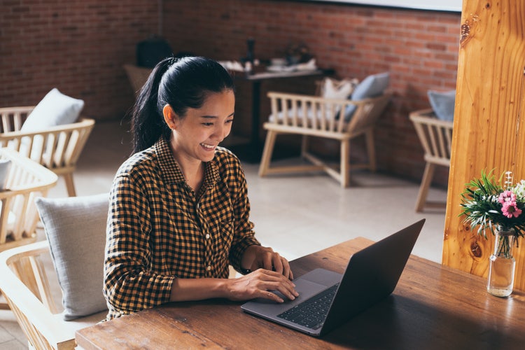 A woman sitting at a table working on a laptop, using the pdf document format.