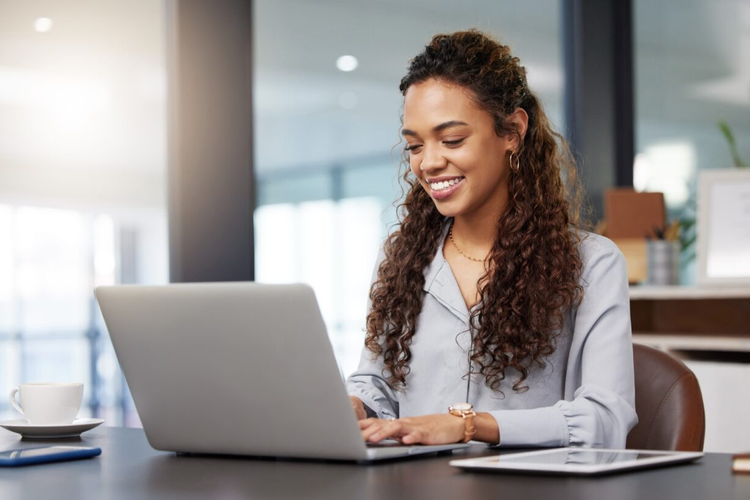 A woman in an office uses her laptop to find the best electronic signature software.