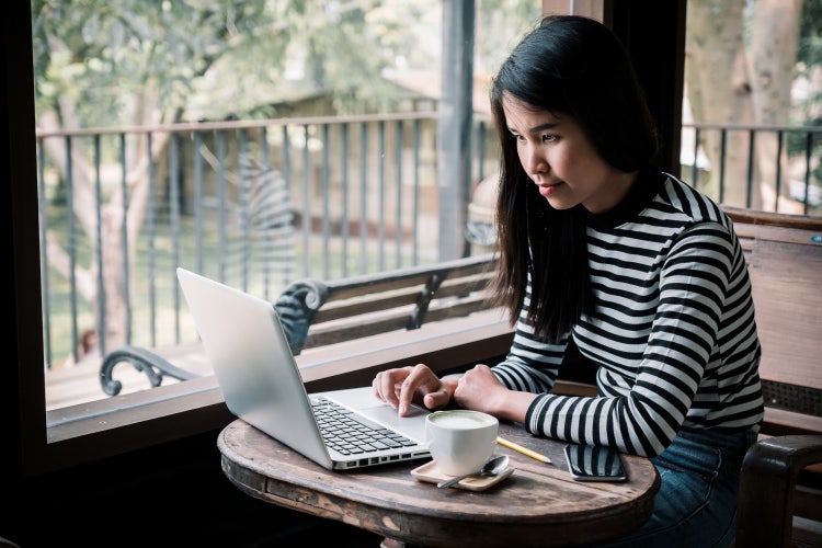 A woman working remotely on her laptop from a coffee shop.