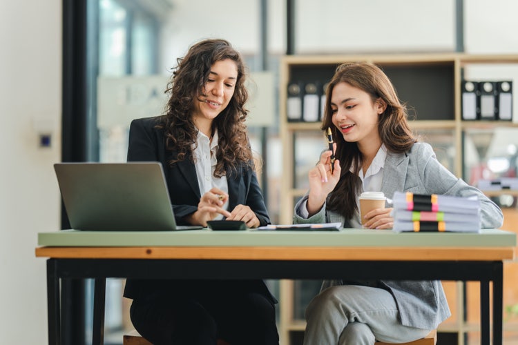 Two women creating a marketing budget plan on a laptop.