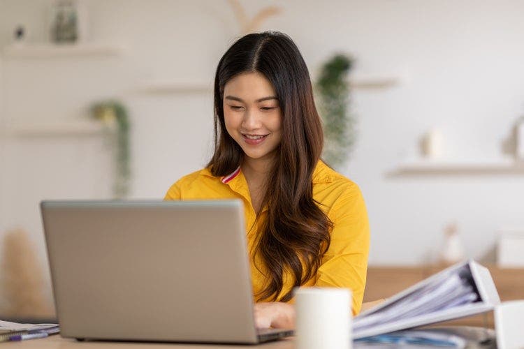 A woman sitting at a table writes on a PDF using 3 simple steps on her laptop.