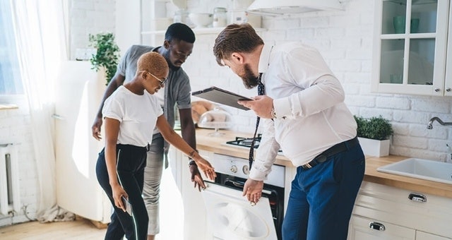 An image of a rental manager and two potential tenants standing in a kitchen and inspecting the oven.