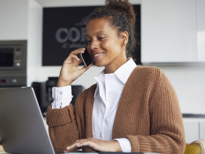 A person sitting at a table using their laptop while talking on their phone