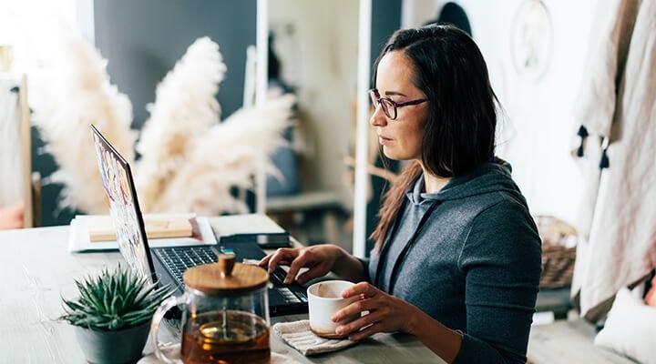 A homeowner sitting at a desk reviewing a real estate contract on their laptop while drinking coffee