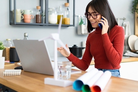 A person sitting at a table using their laptop while talking on their cell phone