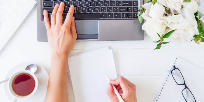 A person takes notes on a piece of paper while working on their computer