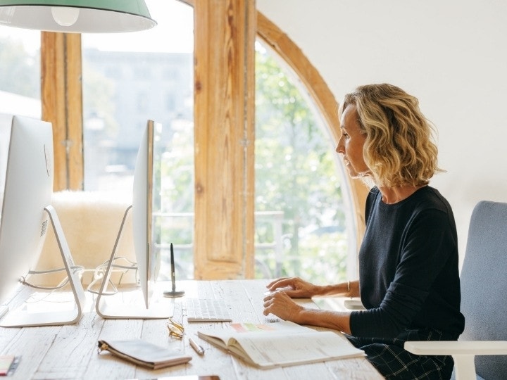 A person sitting at a communal desk working on an iMac to convert a PDF to a JPG using Adobe Acrobat