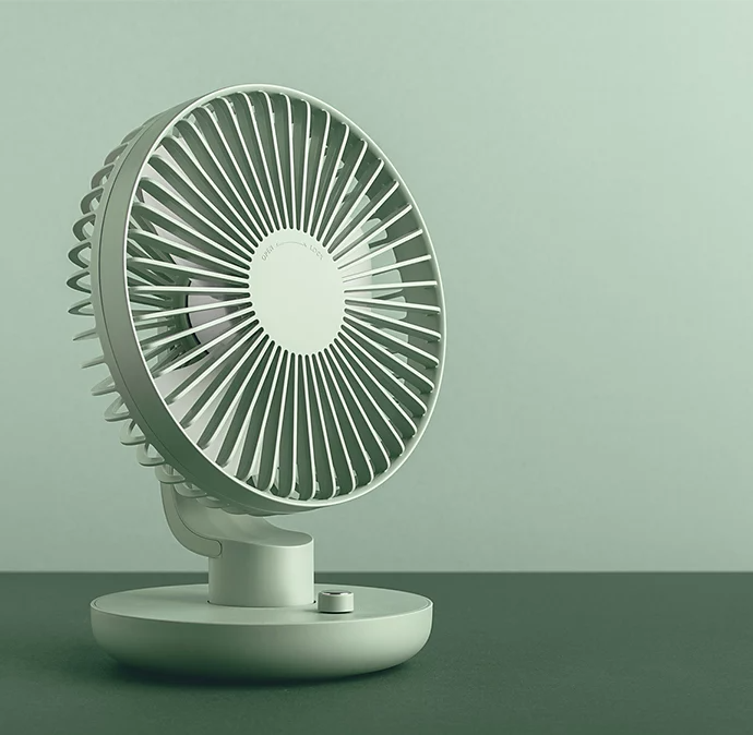 A white fan on a dark surface in front of a white wall