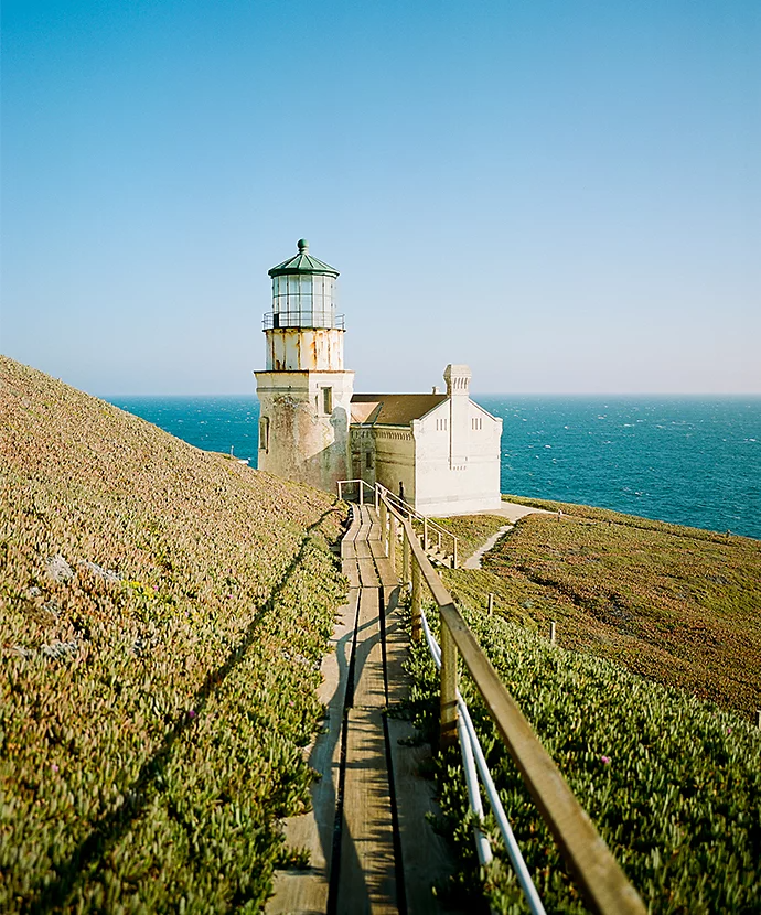 A wooden pathway leading to a lighthouse next to a body of water as an example of perspective photography