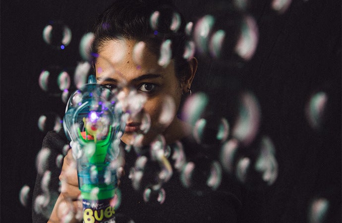 Unique headshot pose of a woman from behind the bubbles of a bubble gun